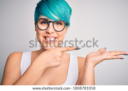 Young beautiful woman with blue fashion hair wearing casual t-shirt and glasses very happy pointing with hand and finger