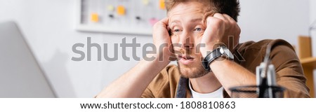 Panoramic shot of tired businessman with hands near head looking at laptop in office 