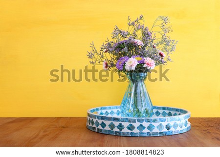 bouquet of colorful field flowers in the glass blue vase over wooden table