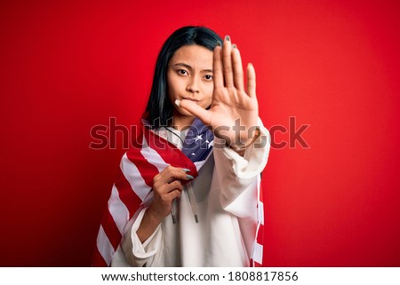 Young beautiful chinese woman wearing United States flag over isolated red background with open hand doing stop sign with serious and confident expression, defense gesture