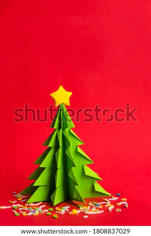 Origami Christmas tree on red background with copy space. Handmade paper tree decorated with sprinkles. Christmas wallpaper.