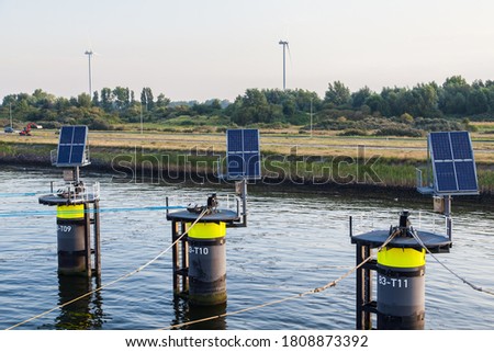 A seaport on the outskirts of Amsterdam with wind generators on the coast and solar panels mounted on mooring posts.
