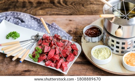 swiss specialty, the fondue bourguignonne with pice of meat and many sauces on wooden table Royalty-Free Stock Photo #1808889670