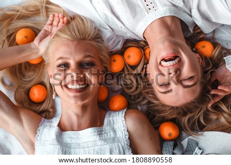 close up portrait of two laughing blonde girls shooting from above. with tangerines