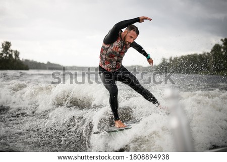 handsome sporty man in wet black swimwear trying to balance on the wave. Wakesurfing on the river. Summertime leisure