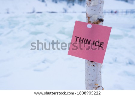 thin ice is written on a piece of paper that is attached to a pole. in winter by the reservoir