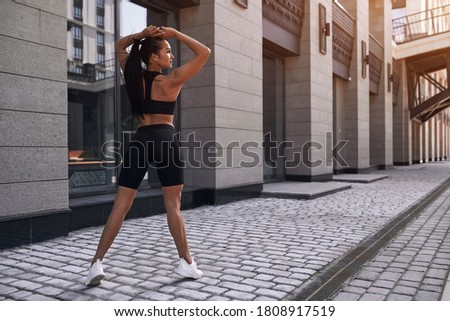 Beautiful woman, summer in city, fitness training on street, posing against window, sportswear. Background glass windows of a building.