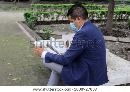 Latino adult man with protection mask, coffee and reading book in the park, new normal covid-19