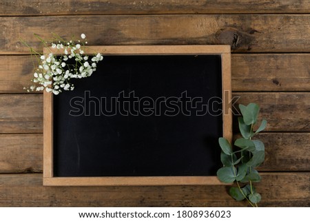Top view of a composition with a black chalkboard, spring of fresh leafs and bunch of flowers, arranged on a textured wooden surface.