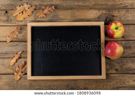 Top view of a composition with a black chalkboard, brown, dried leafs and two apples, arranged on a textured wooden surface.