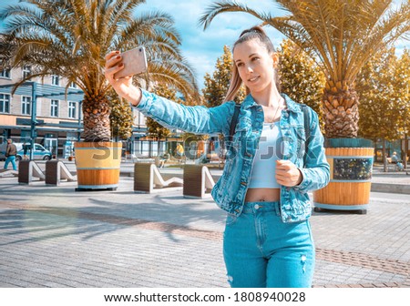 Selfie woman. Happy young girl with phone smile, typing texting and taking selfie in summer sunshine urban city. Pretty female taking fun self portrait photo. Vanity, social network concept.