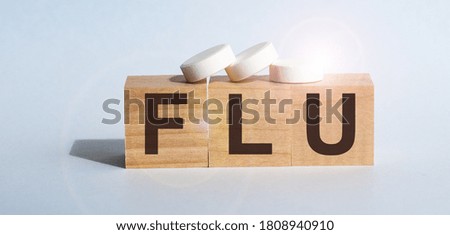 FLU the word on wooden cubes, cubes stand on a gray surface, on cubes - a pills. Medicine concept.