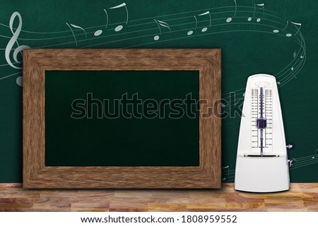 Music class concept with musical notes on background chalkboard and wooden frame copy space next to white mechanical metronome.