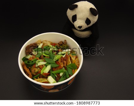 Panda plush with yakisoba japanese food isolated in black background. Copy space,