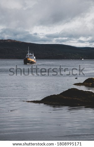 Fishing boat sailing near the rocky shores of Tarbert under dramatic sky. Scotland, UK. Travel destinations, food industry, traditional craft, environmental damage and conservation