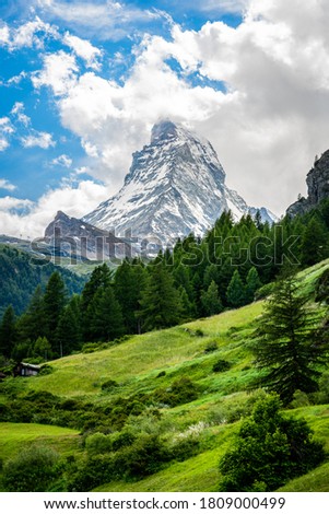 Vertical scenic view of the Matterhorn mountain summit with snow clouds blue sky and green nature during summer in Zermatt Switzerland Royalty-Free Stock Photo #1809000499