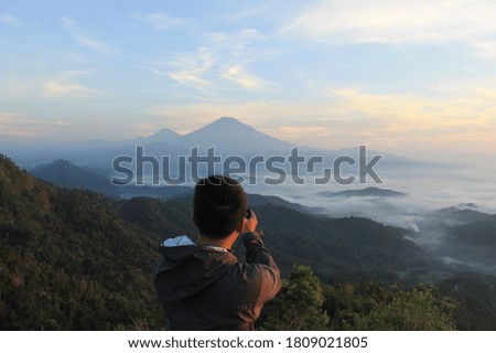 a photographer is capturing the fog covering the area at the foot of the mountain