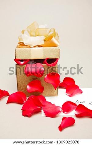 a gold gift box with an open lid and a red flower leaf