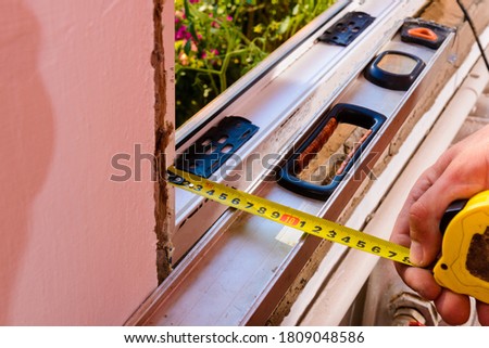 The man performs installation work with the window, for this he also uses a tape measure, measures distances and fastens the window to the wall.