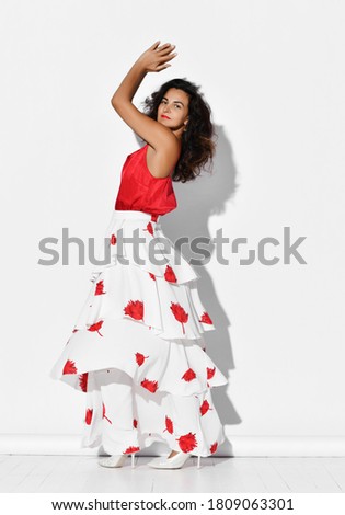 Gorgeous smiling woman hispanic dancer wearing red white gown with flower print dances Carmen flamenco clapping hands up. Fashion vogue style and beauty