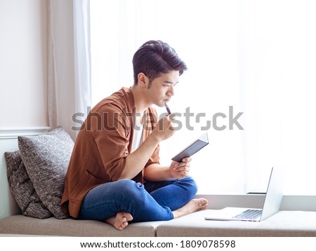 Young asian man writing in notebook and using laptop during COVID-19