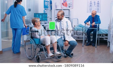 Doctor with green screen tablet in rehabilitation center for elderly disabled patients. Isolated chroma mockup easy replacement for your app, text, video or digital assets. Health care medicine and