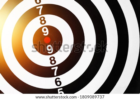 A black and white dart board with red dots is the target.