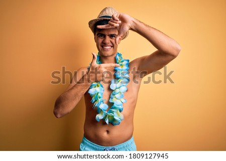 Young handsome tourist man on vacation wearing swimwear and hawaiian lei flowers smiling making frame with hands and fingers with happy face. Creativity and photography concept.
