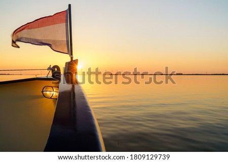 Fore-deck steel boat with Dutch flag during sunset cruise