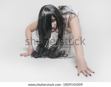 Mystical ghost woman with black hair in white long shirt crawl on gray background