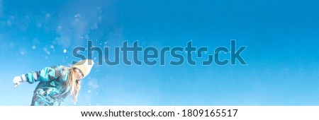 Young teenager girl having fun activity in snow outdoor park. Blue sky background with snowflakes. Banner with copyspace. Blurred defocused stock photo.