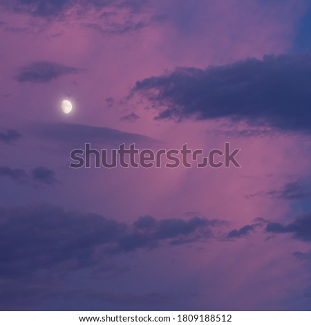 Square photo of the moon lit with very intense blue and pink clouds