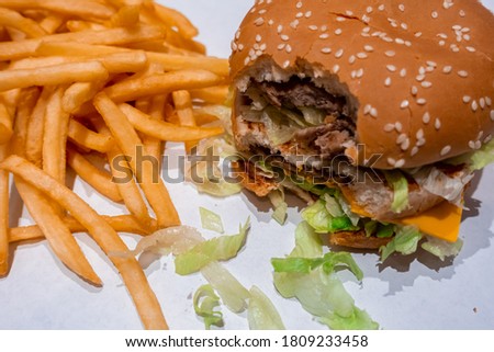 Close up of a bitten double cheeseburger on a tray with freshly cooked french fries inside a fast food restaurant in shopping mall