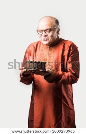 Indian old man celebrating own birthday by blowing candles on cake while wearing ethnic wear