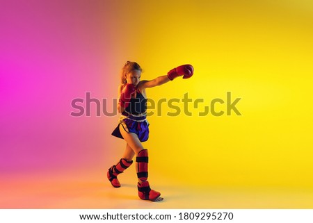 Little caucasian girl, kick boxer on gradient background in neon light, active and expressive. Concept of motion, action, motivation, childhood. Training winner, emotional. Sales, ad, copyspace.