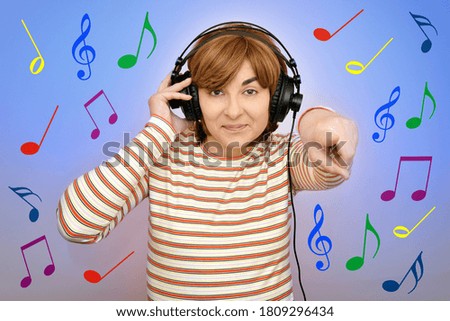 Smiling happy woman with headphones over colorful musical notes background pointing her index finger at the camera