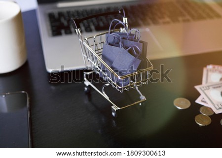 Shopping cart with bags stand on the table near laptop. Black friday. Sale announcement. E-commerce business. Ordering  in the internet store. Sun beams 