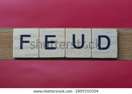 text the word feud from gray wooden small letters with black font on an red table Royalty-Free Stock Photo #1809310504