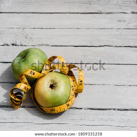 Two yellow and green apples are lying on a white wooden table and wrapped with a yellow centimeter tape. Fitness and healthy lifestyle. Vitamins and minerals, delicious and healthy food.