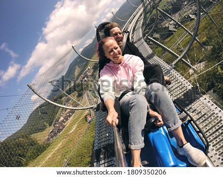 Summer toboggan run rodelbahn with many curves on a mountain. Alpine coaster in summer and autumn beautiful landscapes. Fast ride fun of young couple travelling