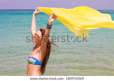 Beautiful young girl holding yellow fabric at wind in beach vacation