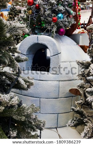Among the green fir trees sprinkled with snow stands a house made of ice bricks - an igloo. North house made of artificial ice bricks.