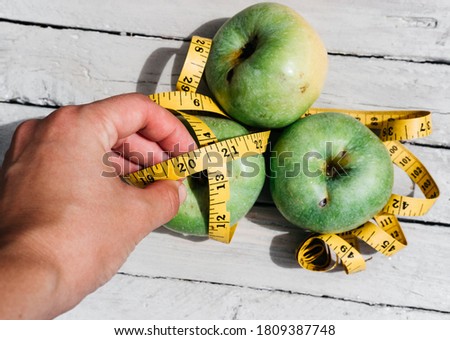 A human touches green fresh apples and a yellow centimeter ribbon with the numbers 2021. Delicious and healthy food with vitamins for fitness and healthy lifestyle.