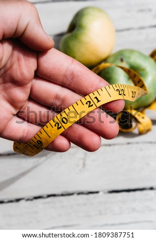 A human touches green fresh apples and a yellow centimeter ribbon with the numbers 2021. Delicious and healthy food with vitamins for fitness and healthy lifestyle.