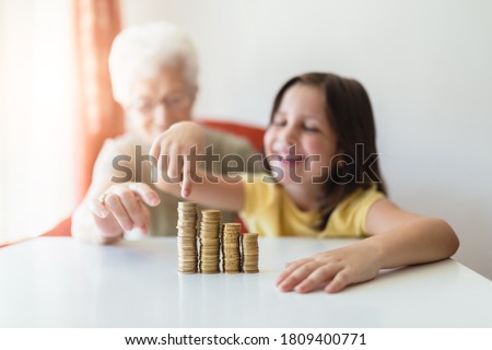 white-haired grandmother with her young granddaughter sitting at home with the savings of the piggy bank