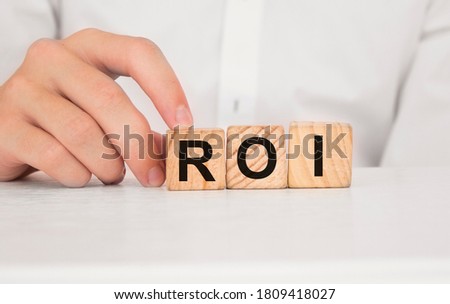 Close up young man's hand in white shirt wooden block cube for Roi wording on white marble table floor