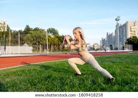 Beautiful young blonde doing lunges exercises during training in the stadium
