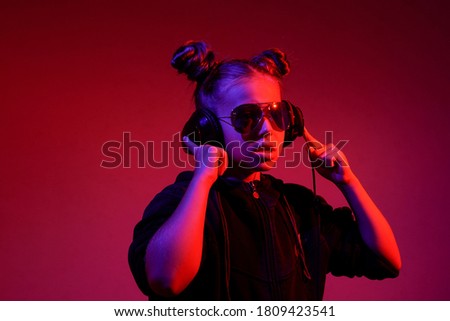 fashionable teenager girl with glasses and headphones listening to music and singing along on a pink background and in blue and red disco lighting