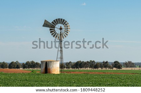 Bore water windmill pump with tank in rural Australia, energy saving equipment for watering and feeding livestock and crops. Royalty-Free Stock Photo #1809448252