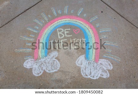 Be the light written with sidewalk chalk with a rainbow